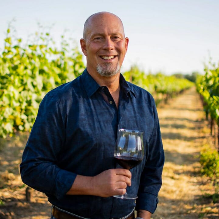 James MacPhail standing in vineyard and holding a glass of red wine