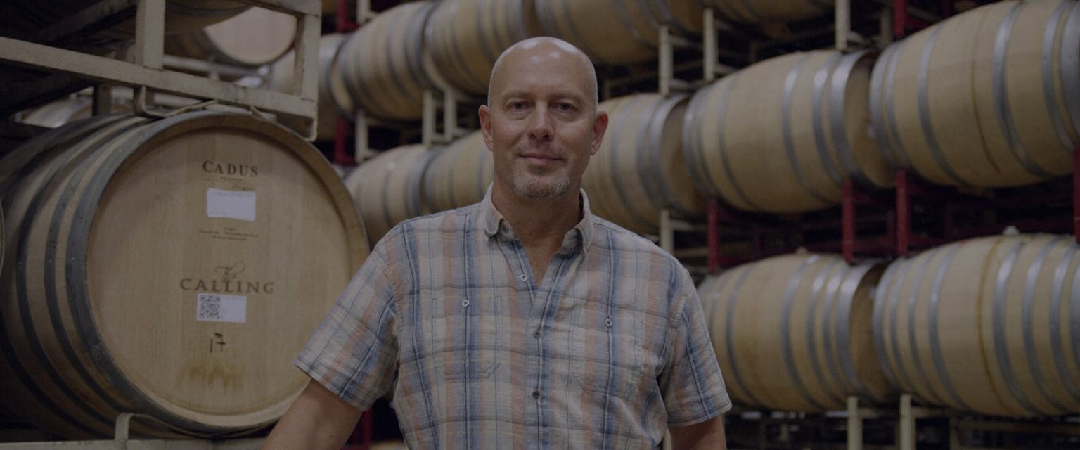 James MacPhail standing in front of barrels of The Calling's wines.